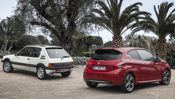 Ein weißer Peugeot 205 und ein roter Peugeot 208 stehen nebeneinander vor Palmen.