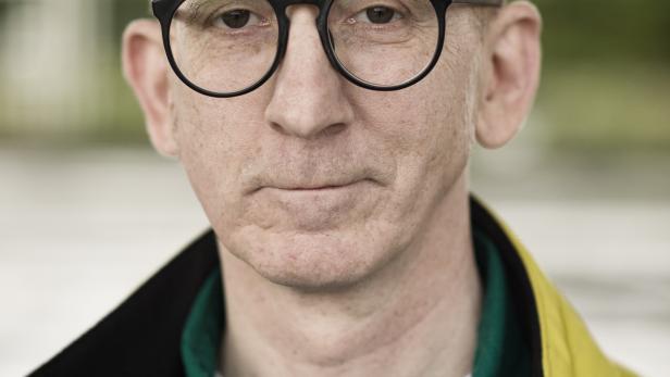 Porträt eines Mannes mit Brille, grünem Hemd und gelber Jacke.