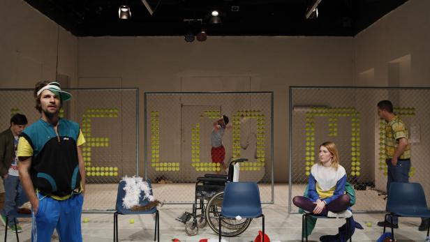 Eine Theaterinszenierung mit Tennisbällen, die ein Wort an einer Gitterwand bilden.
