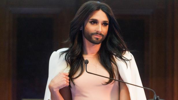 Conchita Wurst steht an einem Rednerpult und spricht.