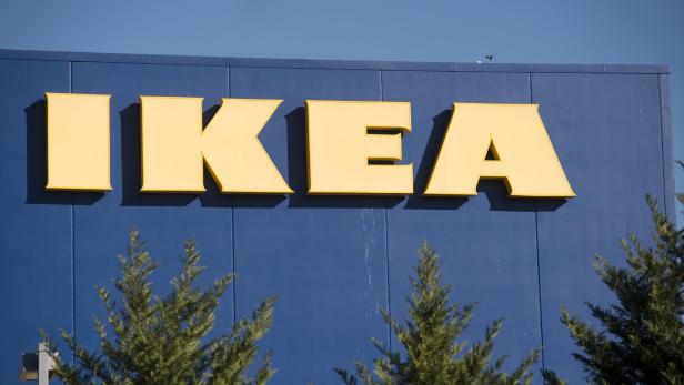 Das gelbe IKEA-Logo an einem blauen Gebäude, teilweise von Bäumen verdeckt.