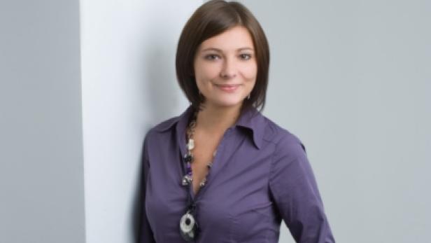 Eine Frau mit braunen Haaren und lila Hemd lächelt in die Kamera.