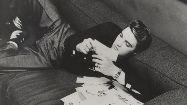 Elvis beim Lesen der Fanpost auf der Couch im Hotelzimmer (1956).