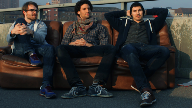 Drei Männer sitzen auf einer braunen Couch im Freien.