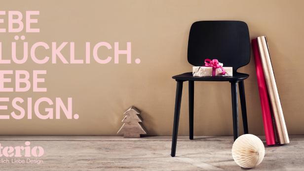 Ein Geschenk mit Schleife liegt auf einem schwarzen Stuhl, daneben Geschenkpapier und Deko-Elemente.