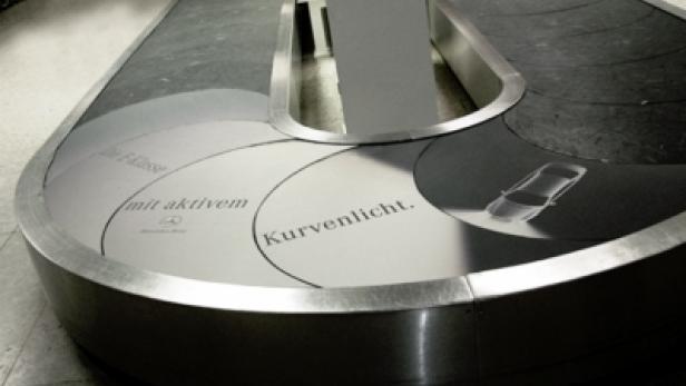 Eine Gepäckausgabe am Flughafen wirbt mit dem Slogan „mit aktivem Kurvenlicht“ für Mercedes-Benz.
