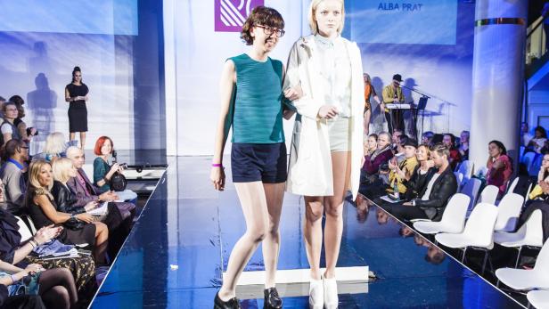 Zwei Frauen präsentieren Mode auf einem Laufsteg vor Publikum.