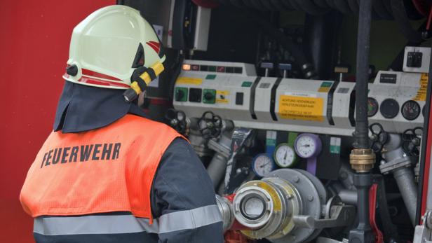 Ein Feuerwehrmann in Schutzkleidung steht an einem Feuerwehrfahrzeug.