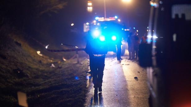 Ein Polizist sichert eine Unfallstelle bei Nacht mit einem Absperrband.