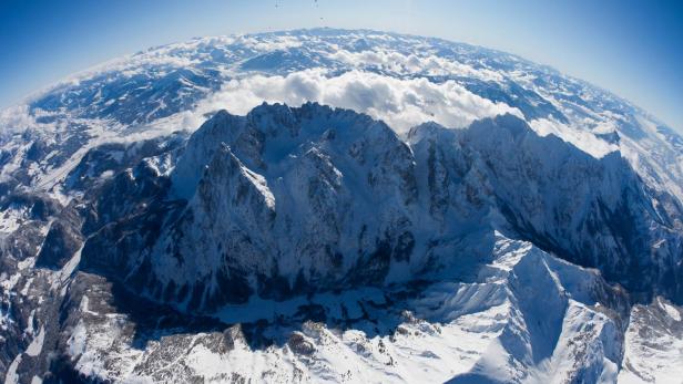 Eine Luftaufnahme einer schneebedeckten Bergkette unter blauem Himmel.
