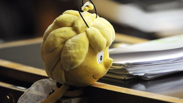 Eine Plüschfigur der Biene Maja steht auf einem Schreibtisch neben einem Stapel Papier.