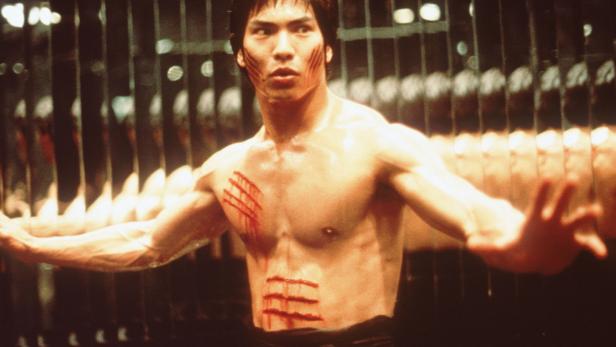 Ein Mann mit Kampfspuren steht vor einem Spiegel.