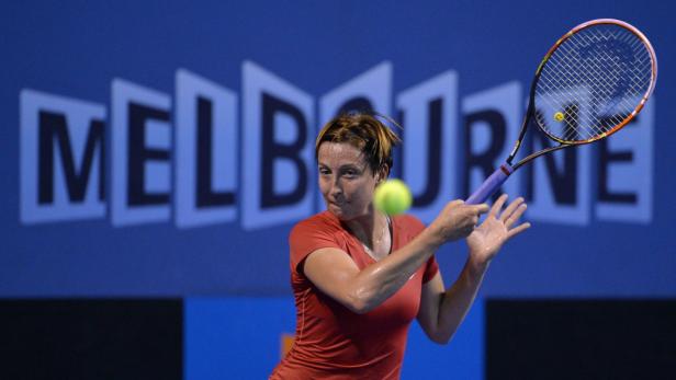 Eine Tennisspielerin schlägt einen Ball vor dem Hintergrund des Melbourne-Schriftzugs.