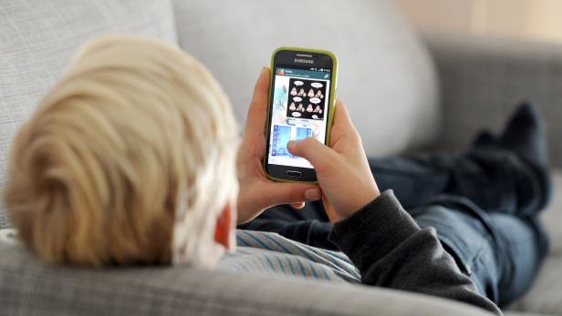 Symbolfoto: Ein Kind auf einer Couch spielt am Handy