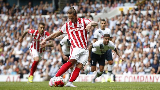 Ein Fußballspieler in rot-weiß gestreiftem Trikot schießt den Ball vor einer Zuschauermenge.