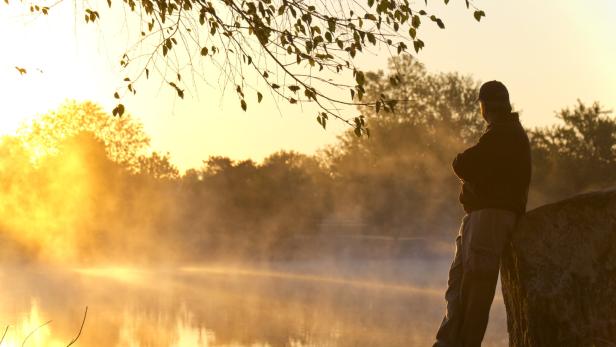 Adult Male Stands Alone At Sunrise Staring Towards Foggy Lake