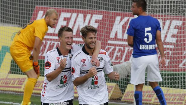 Zwei jubelnde Fußballspieler in weißen Trikots umarmen sich auf dem Spielfeld.