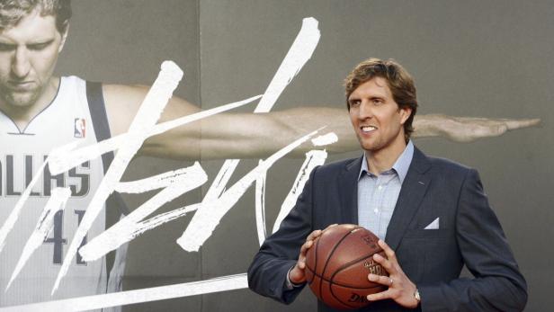 Dirk Nowitzki posiert mit einem Basketball vor einem Poster von sich selbst.