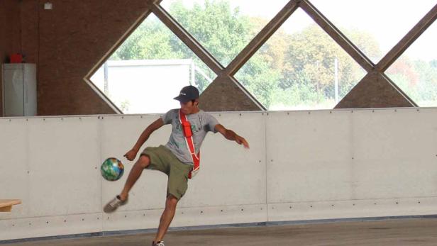 Ein junger Mann jongliert mit einem Fußball in einer Halle.