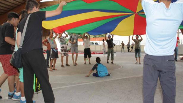 Eine Gruppe von Jugendlichen hält ein buntes Schwungtuch in einer Turnhalle hoch.