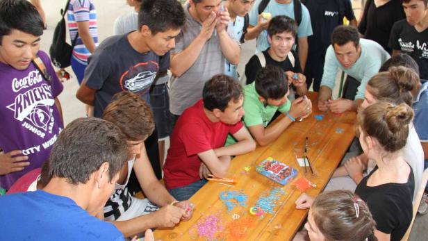 Eine Gruppe junger Leute bastelt gemeinsam an einem Tisch mit bunten Gummibändern.