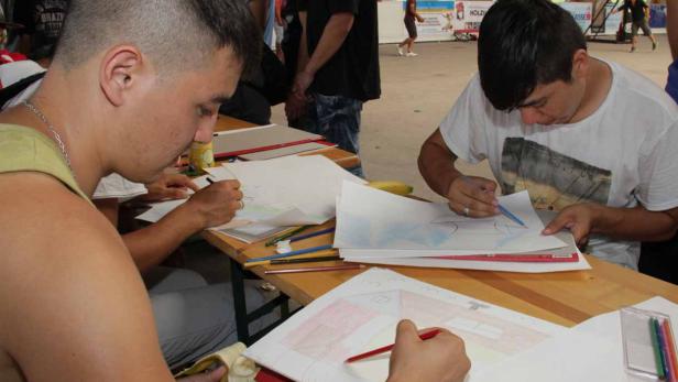 Mehrere Personen sitzen an Tischen und zeichnen mit Buntstiften auf Papier.