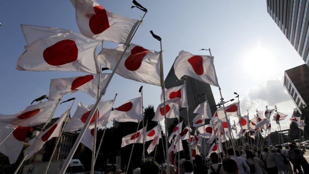 Viele japanische Flaggen wehen im Wind vor dem Hintergrund von Gebäuden und Menschen.