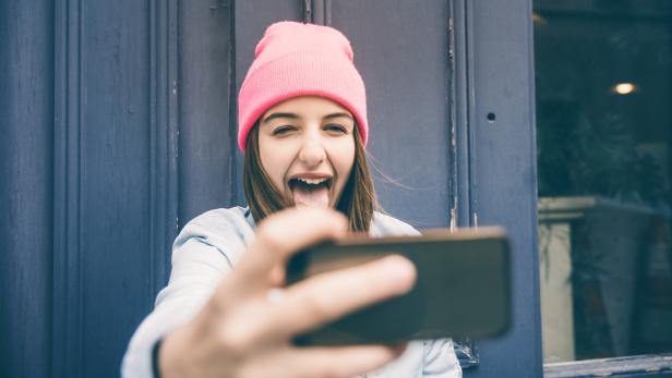 Ein Teenager-Mädchen macht ein Selfie und schneidet Grimassen.