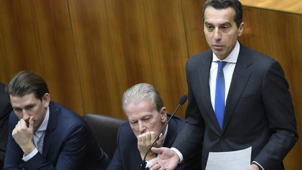 Ein Mann in einem Anzug spricht vor zwei anderen Männern in einem Raum mit Holzvertäfelung.