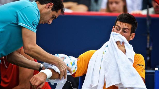 Novak Đoković wird während eines Tennisspiels von einem Betreuer behandelt.