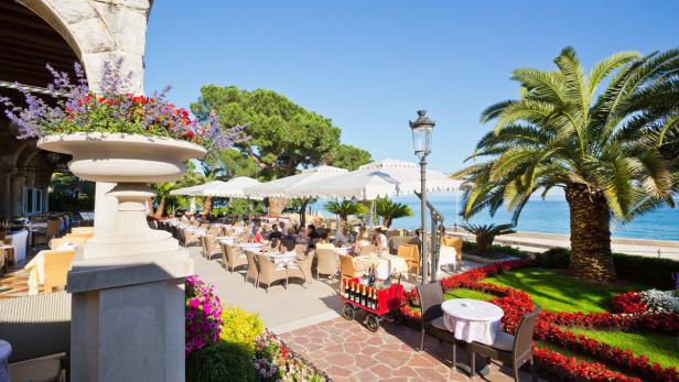 Ein Restaurant im Freien mit Tischen, Sonnenschirmen und Blick auf das Meer.