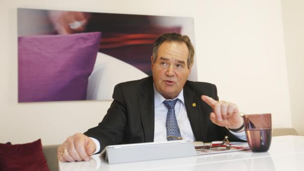 Ein Mann im Anzug sitzt an einem Tisch und gestikuliert.