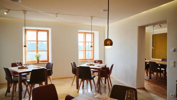 Einladender Gastraum mit gedeckten Holztischen und großen Fenstern.