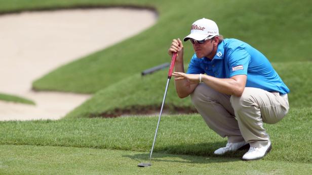 Ein Golfspieler hockt auf dem Grün und visiert den Putt an.