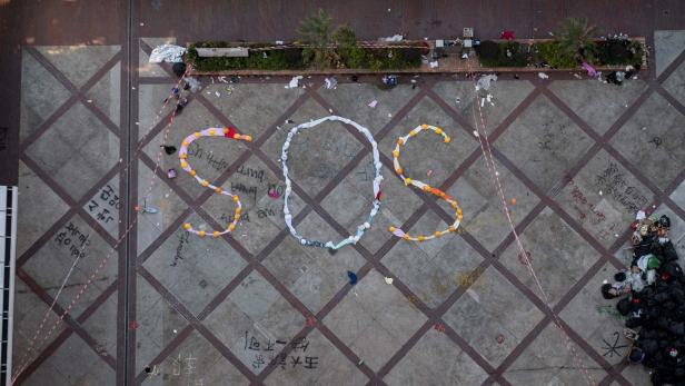 Aus der Vogelperspektive zeigt ein Platz mit der Aufschrift „SOS“ aus Müll und Graffiti.