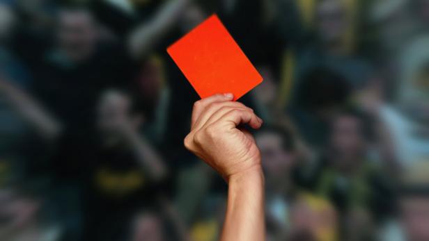 A hand holding a red card up in front of a blurred crowd