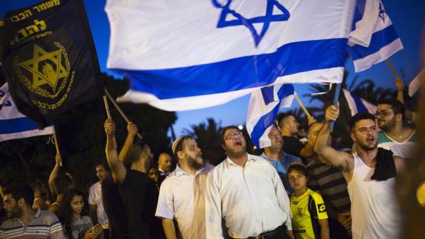 Eine Menschenmenge demonstriert mit israelischen Flaggen und einer schwarzen Flagge mit Davidstern.
