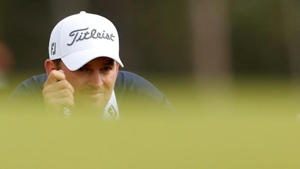 Ein Golfspieler mit einer weißen Kappe der Marke Titleist schaut konzentriert auf das Grün.