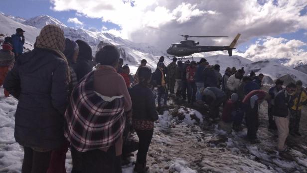 Eine Menschenmenge steht vor einer Bergkulisse, während ein Hubschrauber landet.