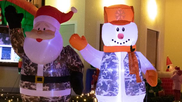 Ein beleuchteter Weihnachtsmann und Schneemann in Tarnkleidung stehen auf einem Rasen mit Lichtern.
