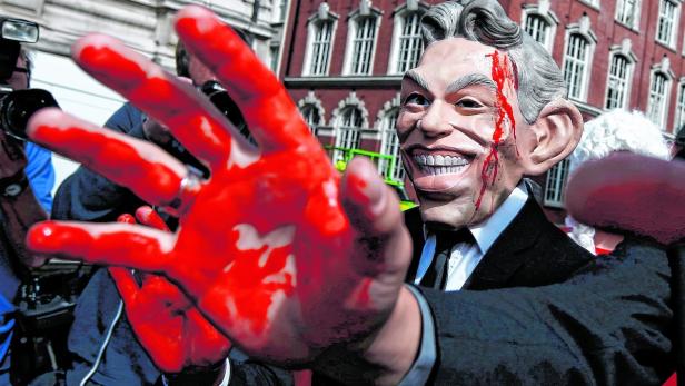 Eine Person mit einer Tony-Blair-Maske und blutverschmierten Händen bei einer Demonstration.