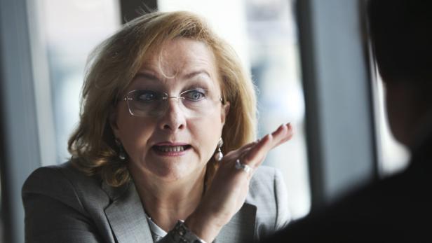 Eine Frau in einem grauen Blazer gestikuliert während eines Gesprächs.
