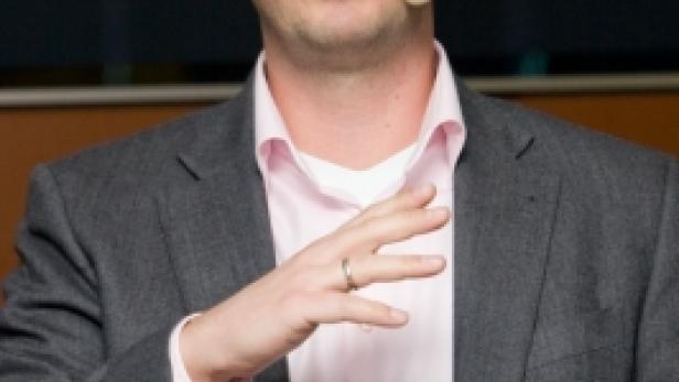 Ein Mann mit Brille und Mikrofon gestikuliert während einer Präsentation.