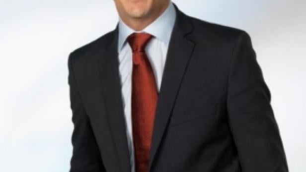 Ein Mann im Anzug mit roter Krawatte lächelt in die Kamera.