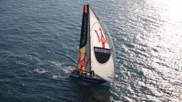 Ein Segelboot der Marke Maserati segelt auf dem glitzernden Meer.