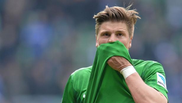 Ein Fußballspieler verdeckt sein Gesicht mit einem grünen Trikot.