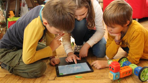 Drei Kinder vor einem Tablet auf dem Boden und einem selbst zusammengebauten Roboter