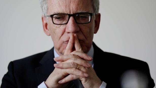 Ein Mann mit Brille und Anzug hält die Hände vors Gesicht und wirkt nachdenklich.