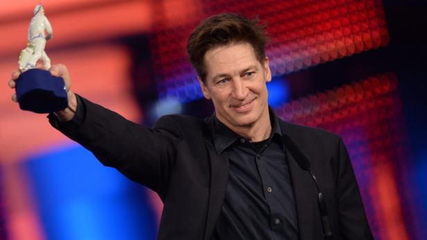 Til Schweiger hält eine Porzellanfigur in die Höhe.