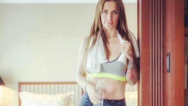 Eine Frau in Sportkleidung und mit einem Handtuch um den Hals hält eine Wasserflasche.